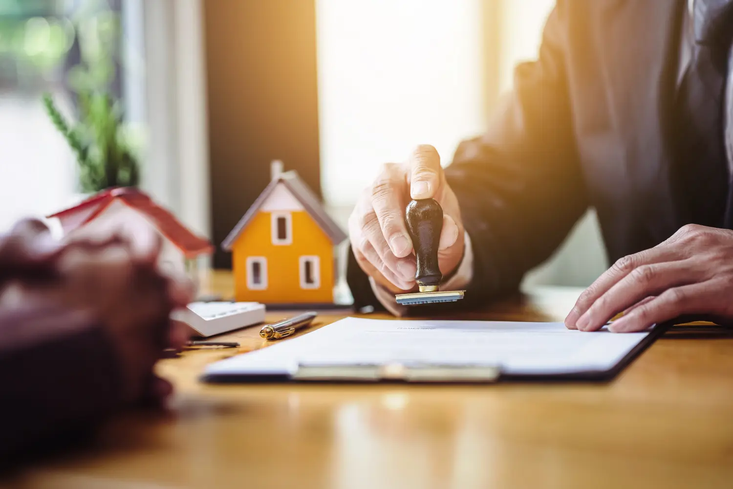 Nahaufnahme der Hand eines Immobilienmaklers, der einen Stempel hält, um die Dokumente für den Immobilienkauf abzustempeln. 